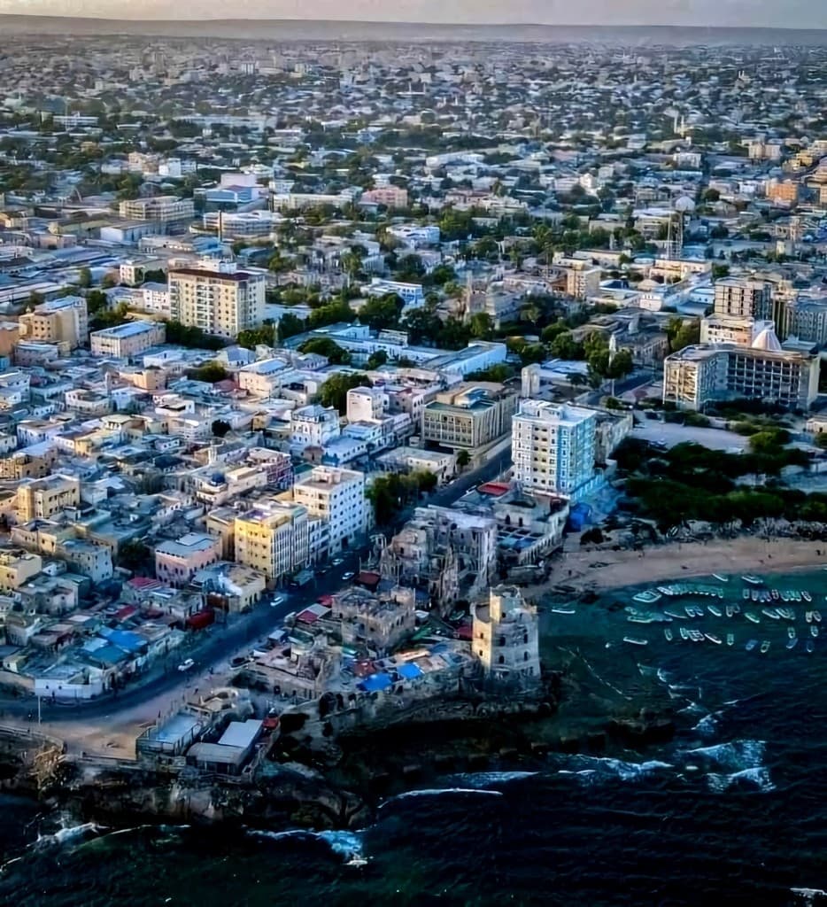 Aerial view of the Mogadishu coastline with the historic lighthouse, dense cityscape, and boats in the harbor.